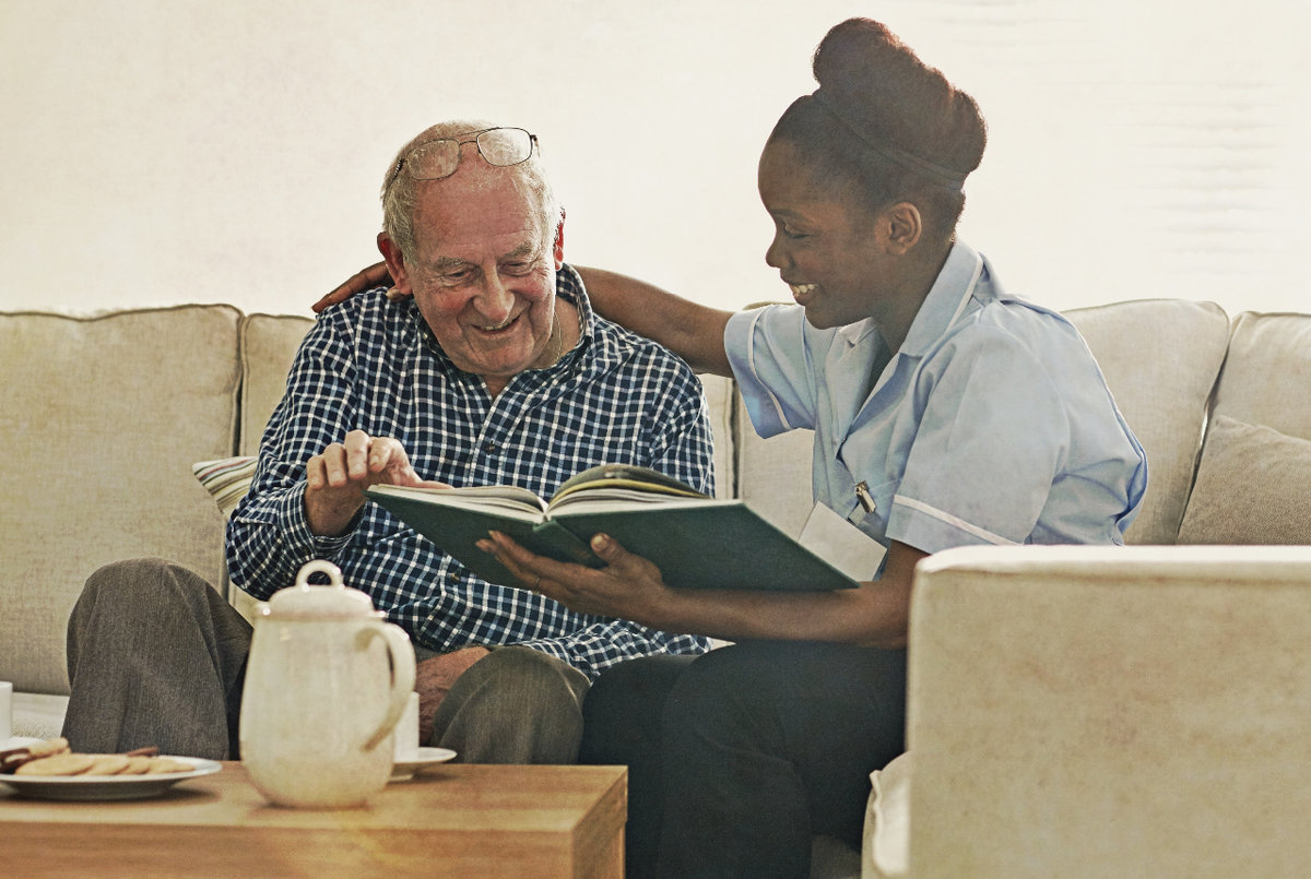 female caregiver reading a book with an elderly male client